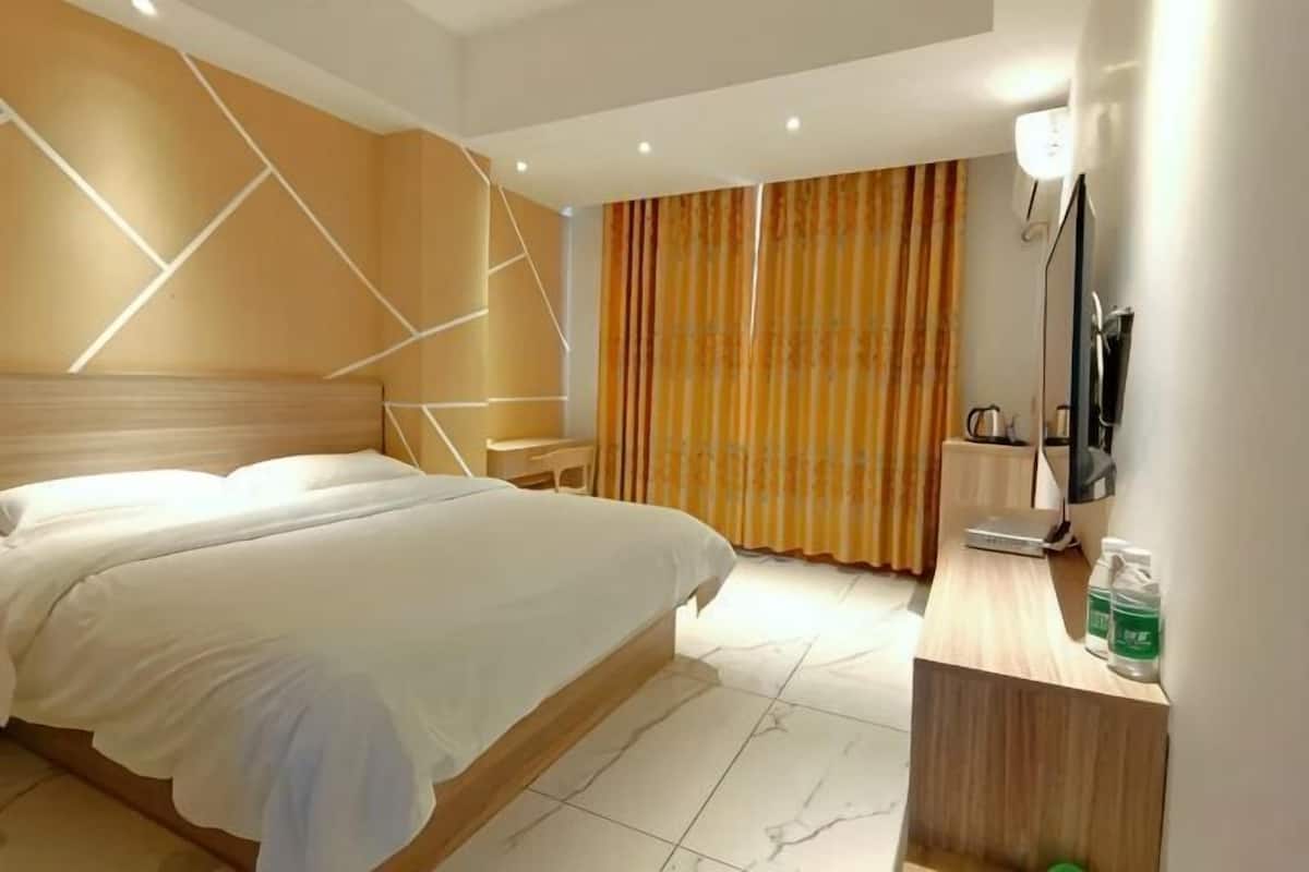 Habitación de hotel con una cama grande, un escritorio con una silla, un televisor y una cortina.