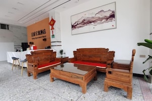 Un área de recepción con mostrador, dos sofás de madera, una mesa de centro y una obra de arte en la pared.