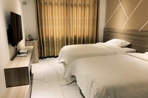 Habitación de hotel con dos camas, televisión, escritorio y ventana con cortinas.