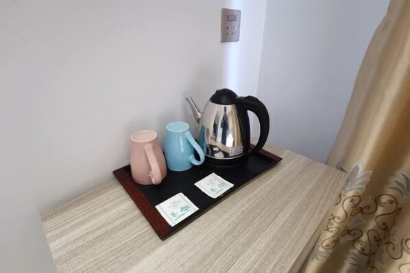 Une petite table sur laquelle se trouve un plateau noir portant une tasse rose, une tasse bleue et une bouilloire électrique argentée. Deux petites cartes sont posées sur le plateau.