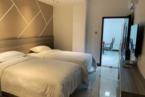 Habitación de hotel con dos camas, cabecero de madera, televisor de pantalla plana y puerta que da a un balcón.