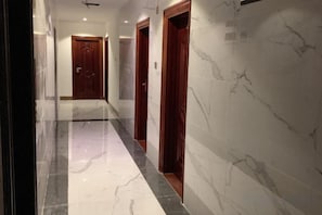 Un pasillo con paredes de mármol y puertas, que conduce a una habitación con puerta de madera.