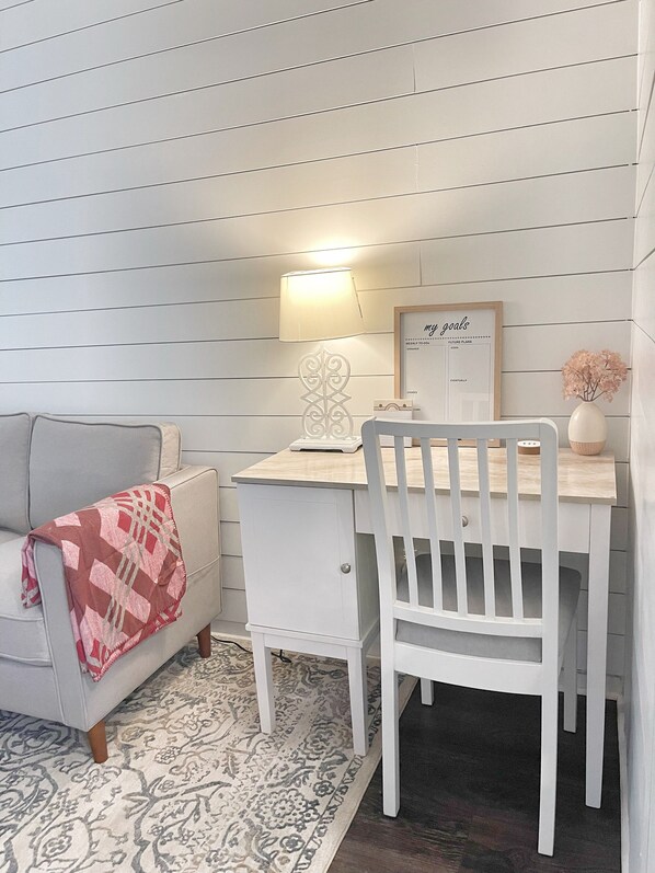 Une pièce confortable avec un bureau blanc, une chaise, une lampe, un tableau encadré sur lequel sont affichés des objectifs, et un tapis à motifs.