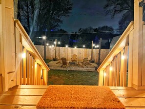 Une terrasse en bois avec un banc, un foyer et des guirlandes lumineuses.