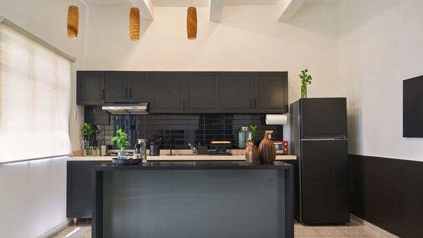 Une cuisine moderne avec des meubles de couleur sombre, un îlot central et un réfrigérateur noir.