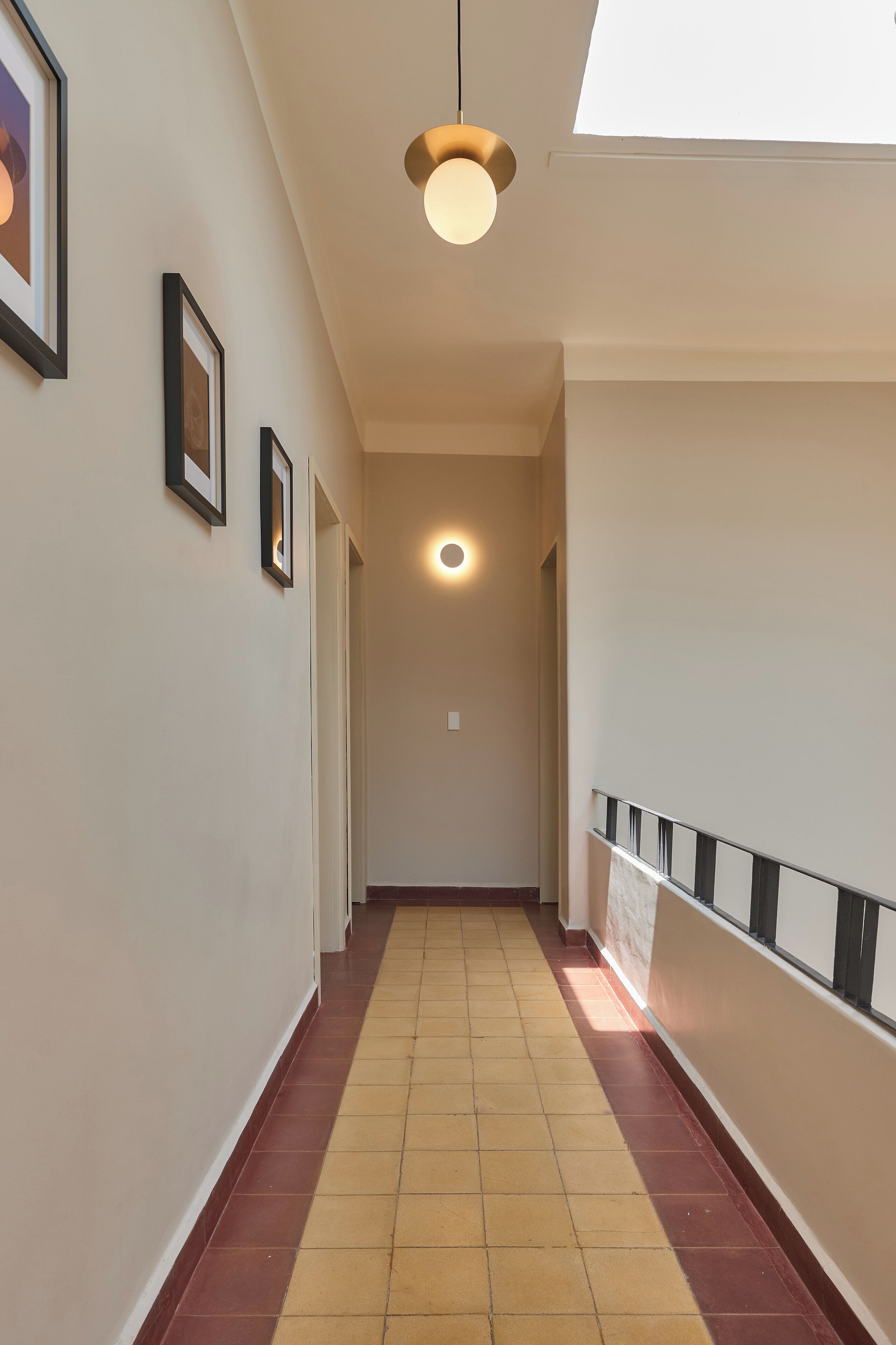 A corridor with framed pictures on the wall, a ceiling light, and a tiled floor.