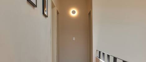 A corridor with framed pictures on the wall, a ceiling light, and a tiled floor.