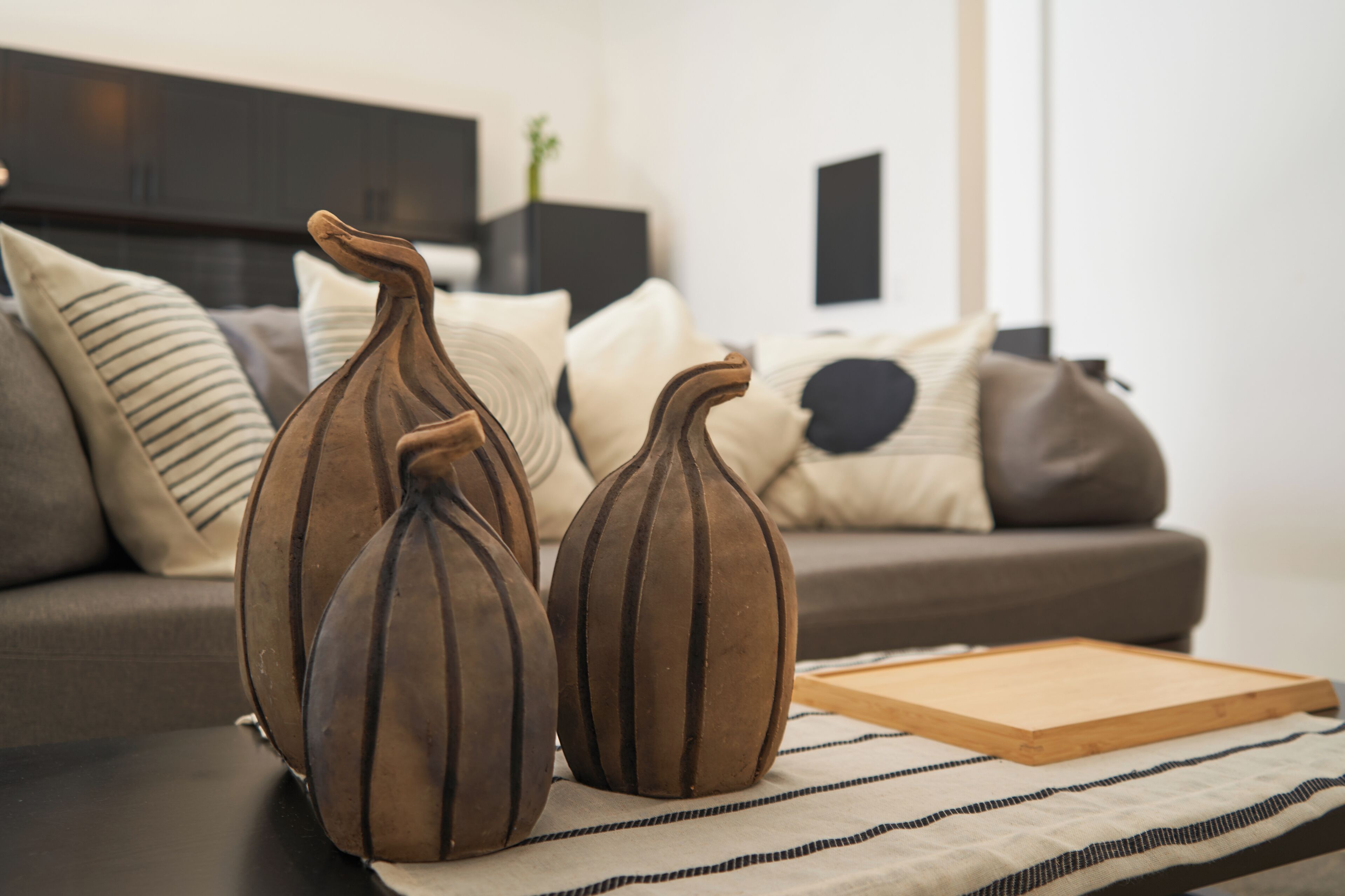 Three vases on a table in a living room with a sofa and pillows in the background.