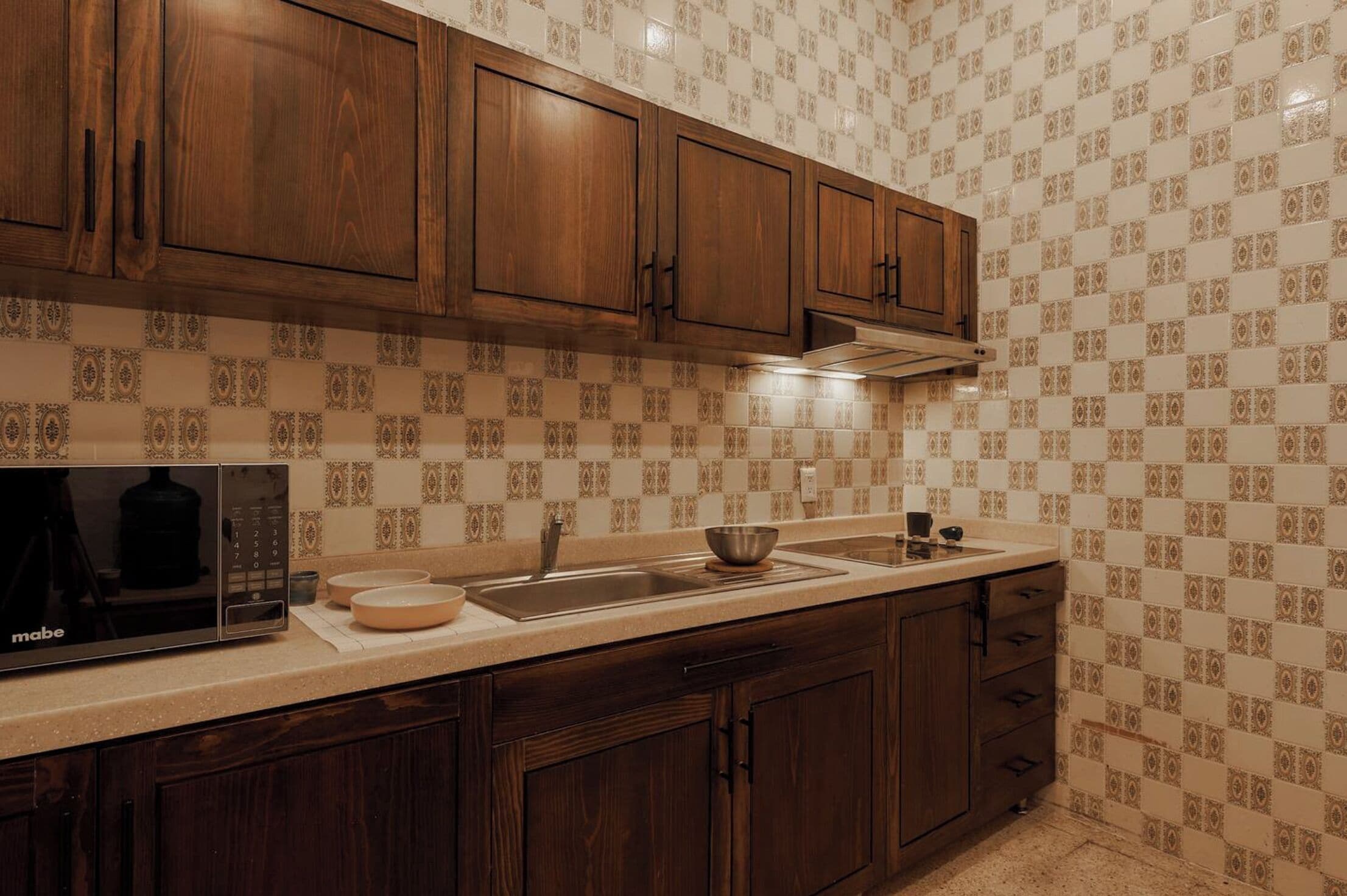 Une cuisine avec des meubles en bois, un four à micro-ondes, un évier et des carreaux décoratifs sur le mur derrière l’évier.