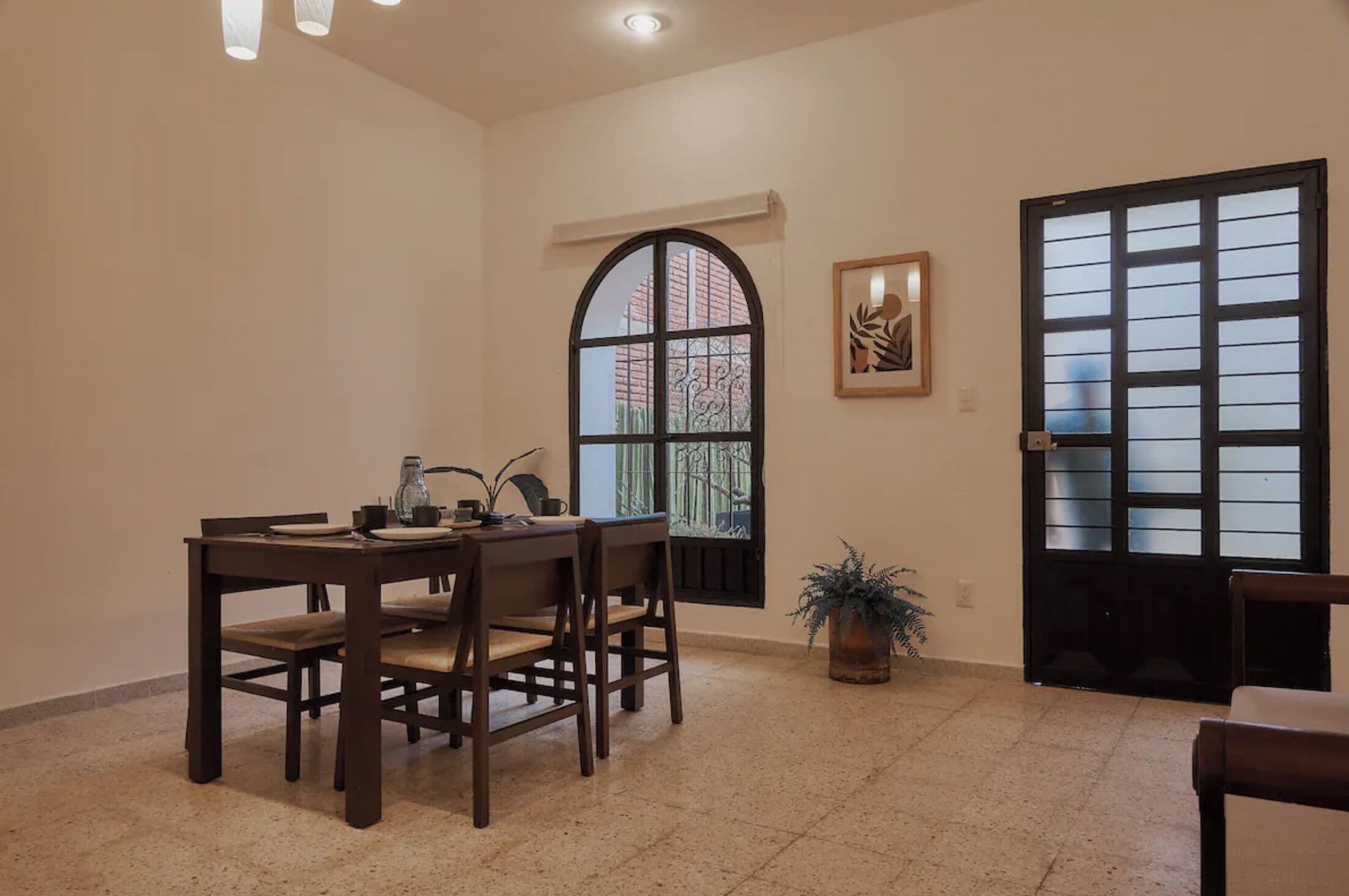 A dining area with a table and chairs, a window with a view, a door with a window, and a framed picture on the wall.