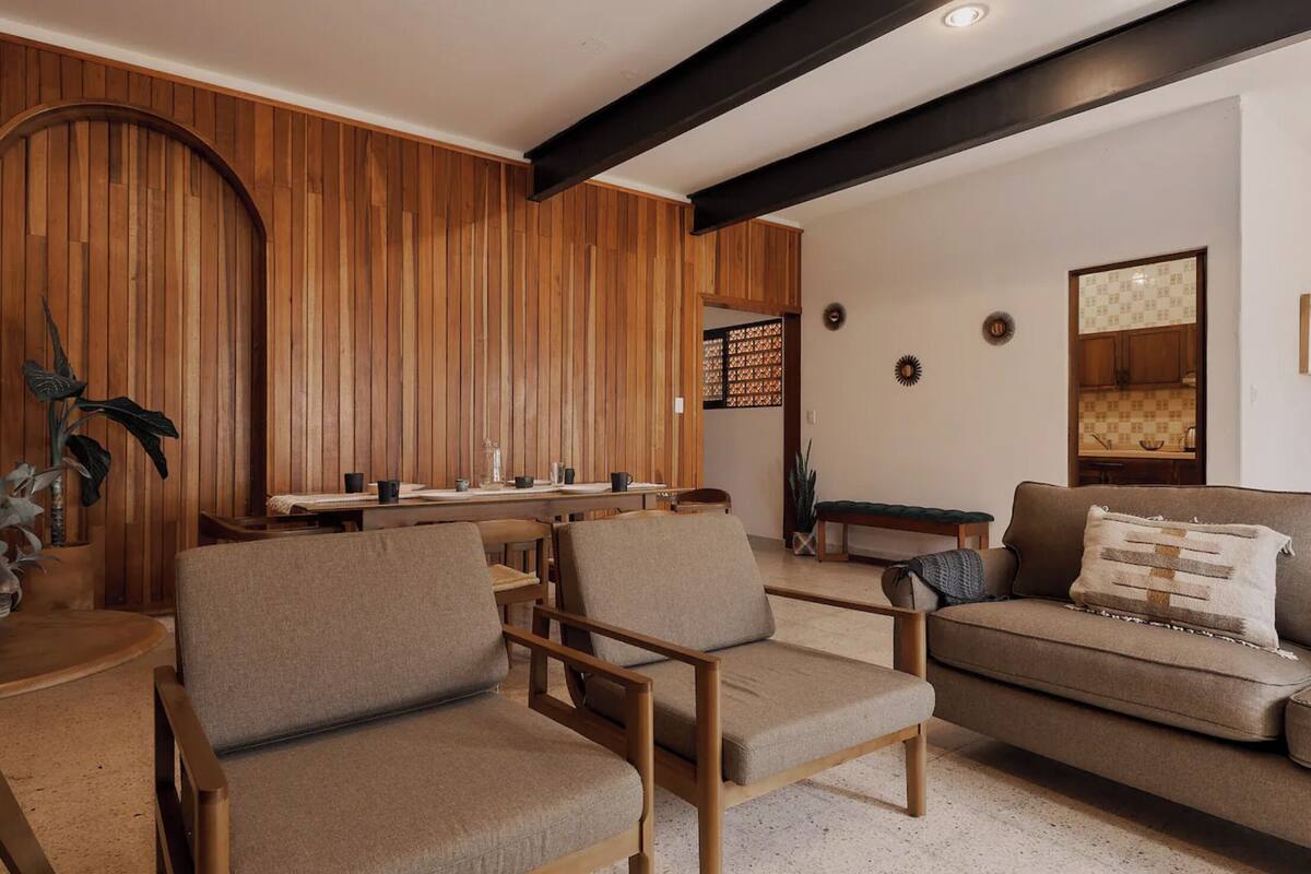 A modern living room with wooden paneling, a sofa, and two armchairs.