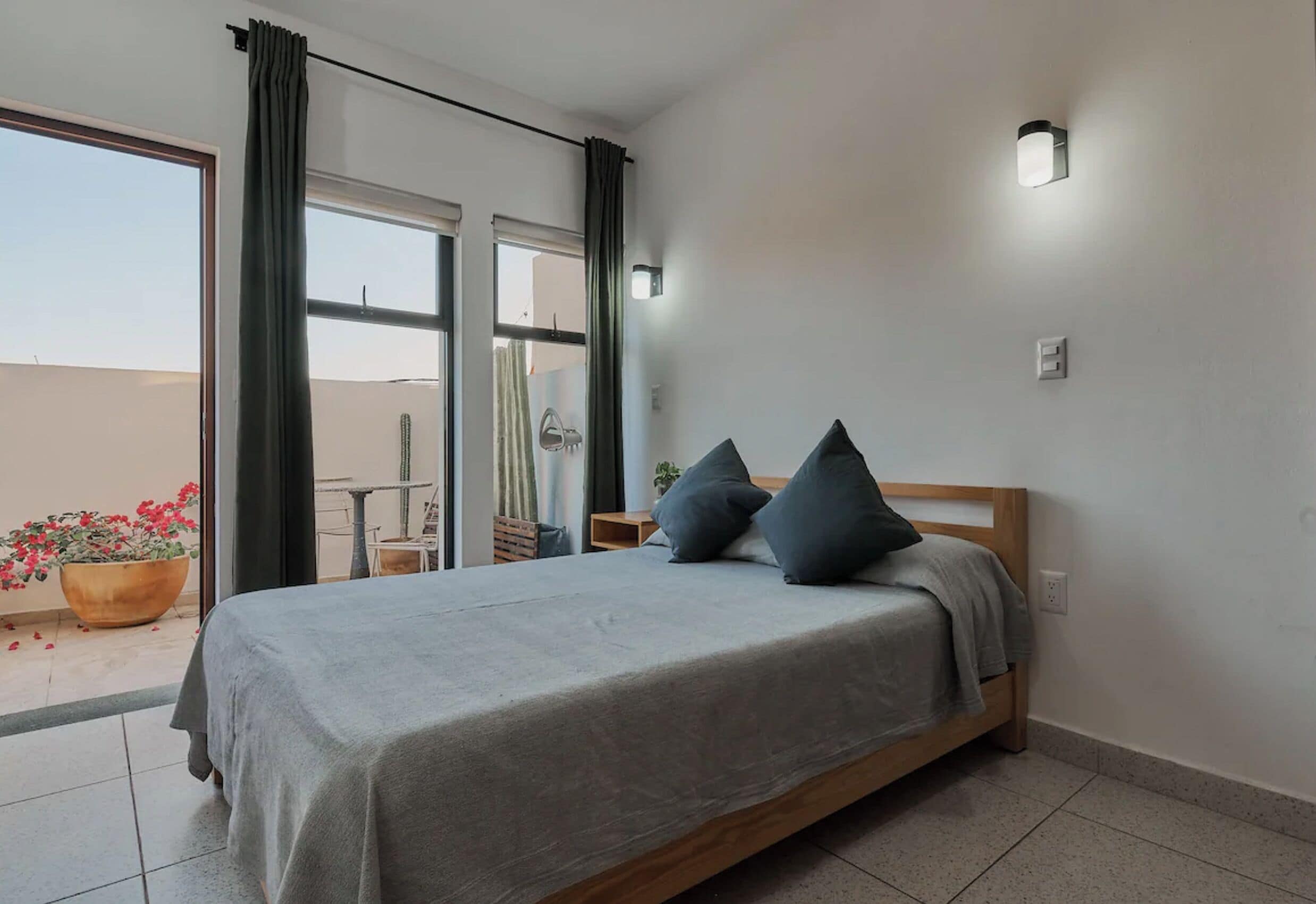 Une chambre à coucher avec un lit, une table de chevet, une plante en pot et une vue sur l’extérieur.