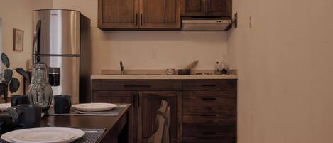 A modern kitchen with wooden cabinets, a stainless steel refrigerator, and a dining table set with plates and cups.