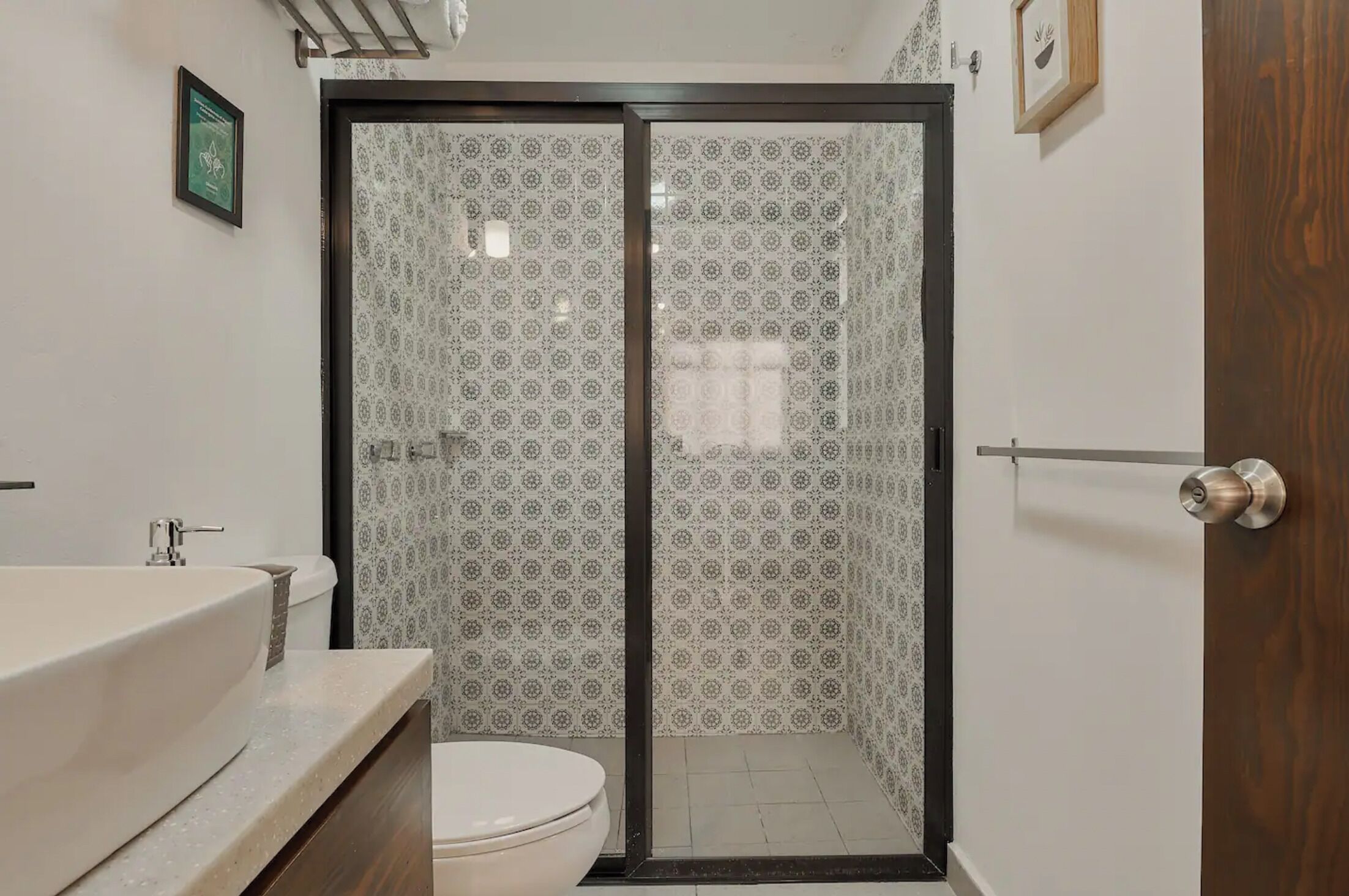 A bathroom with a toilet, sink, and shower area with patterned tiles.