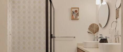Ein modernes Badezimmer mit Dusche, zwei Waschbecken, einem großen Spiegel und einem gerahmten Kunstwerk an der Wand.