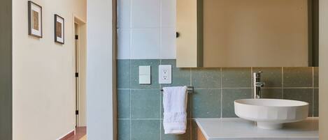 Un baño con lavamanos blanco, tocador de madera y azulejos color turquesa.