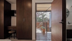Une chambre à coucher comprenant un lit, un bureau, une chaise et une armoire. Il y a un balcon avec des plantes en pot et une vue sur l’extérieur.