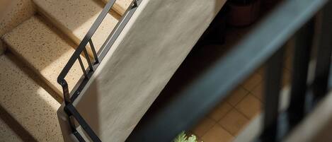 A staircase with a handrail, a tiled floor, and potted plants at the bottom.