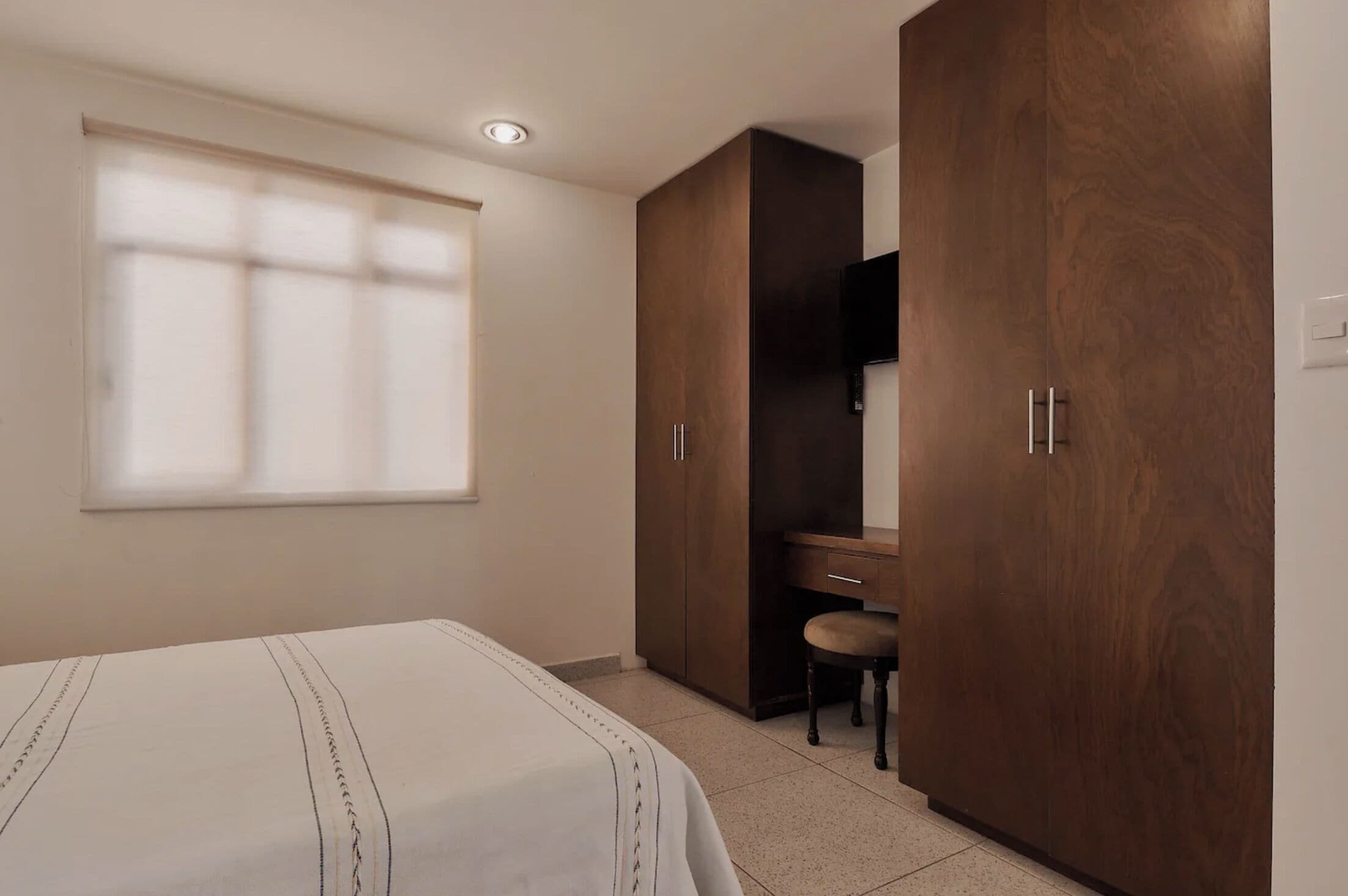 A bedroom with a bed, a desk, and a wardrobe.