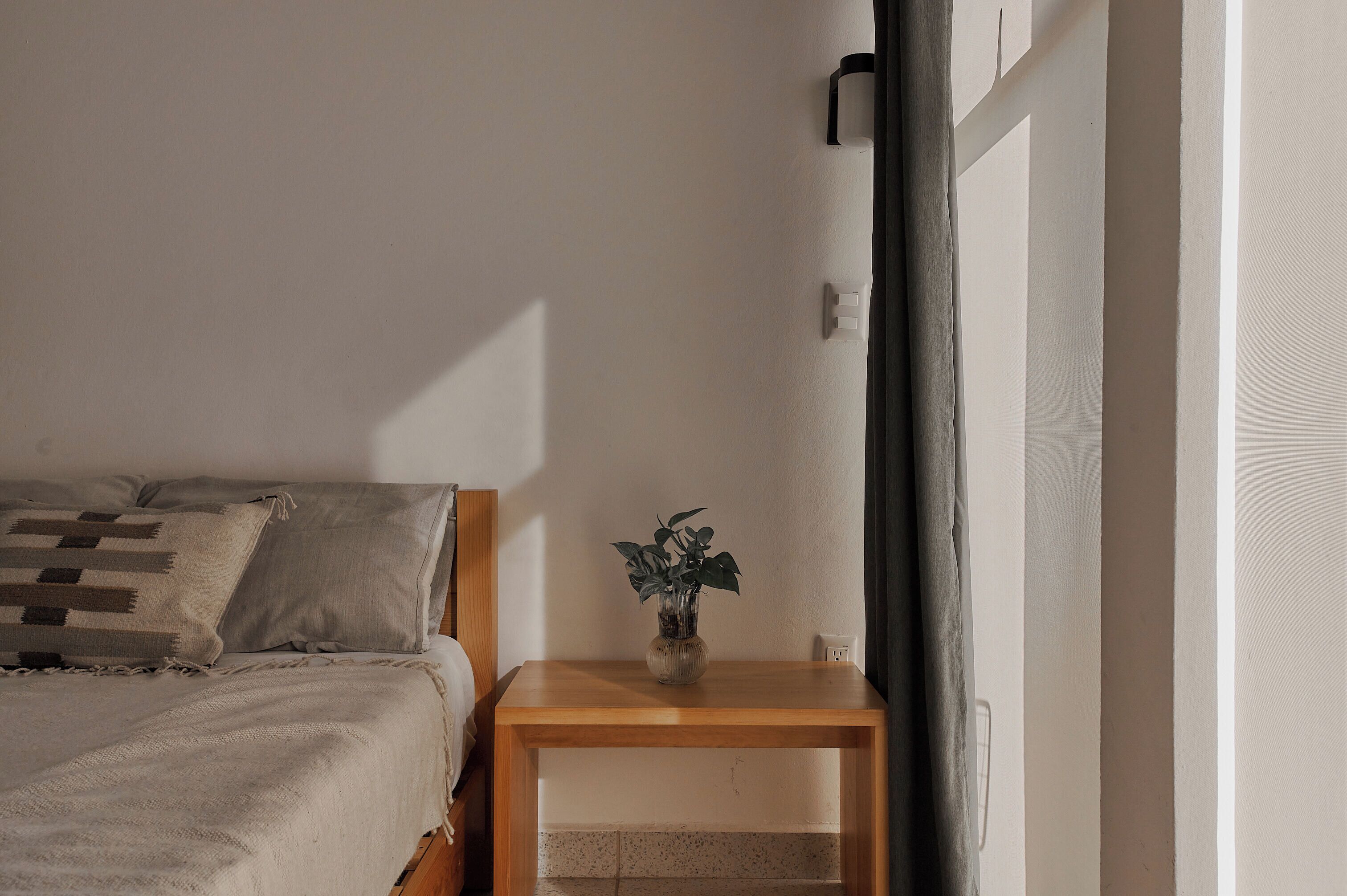 Ein Schlafzimmer mit einem Bett, einem Nachttisch mit Pflanze und einer Wandleuchte.