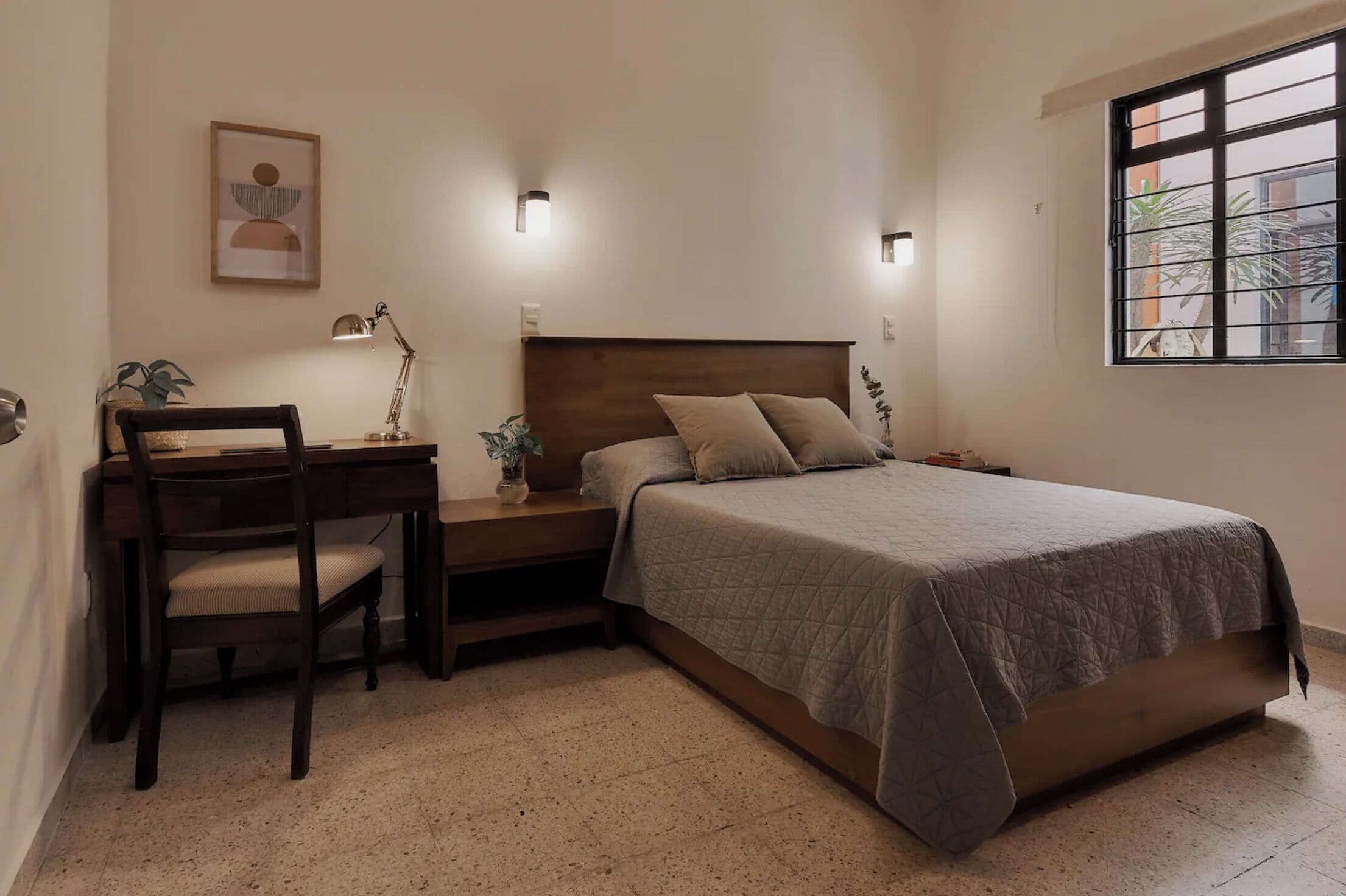 A bedroom with a bed, desk, chair, and bedside lamps.