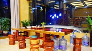 Un área de recepción con un mostrador de madera, plantas en macetas y botellas de agua apiladas.