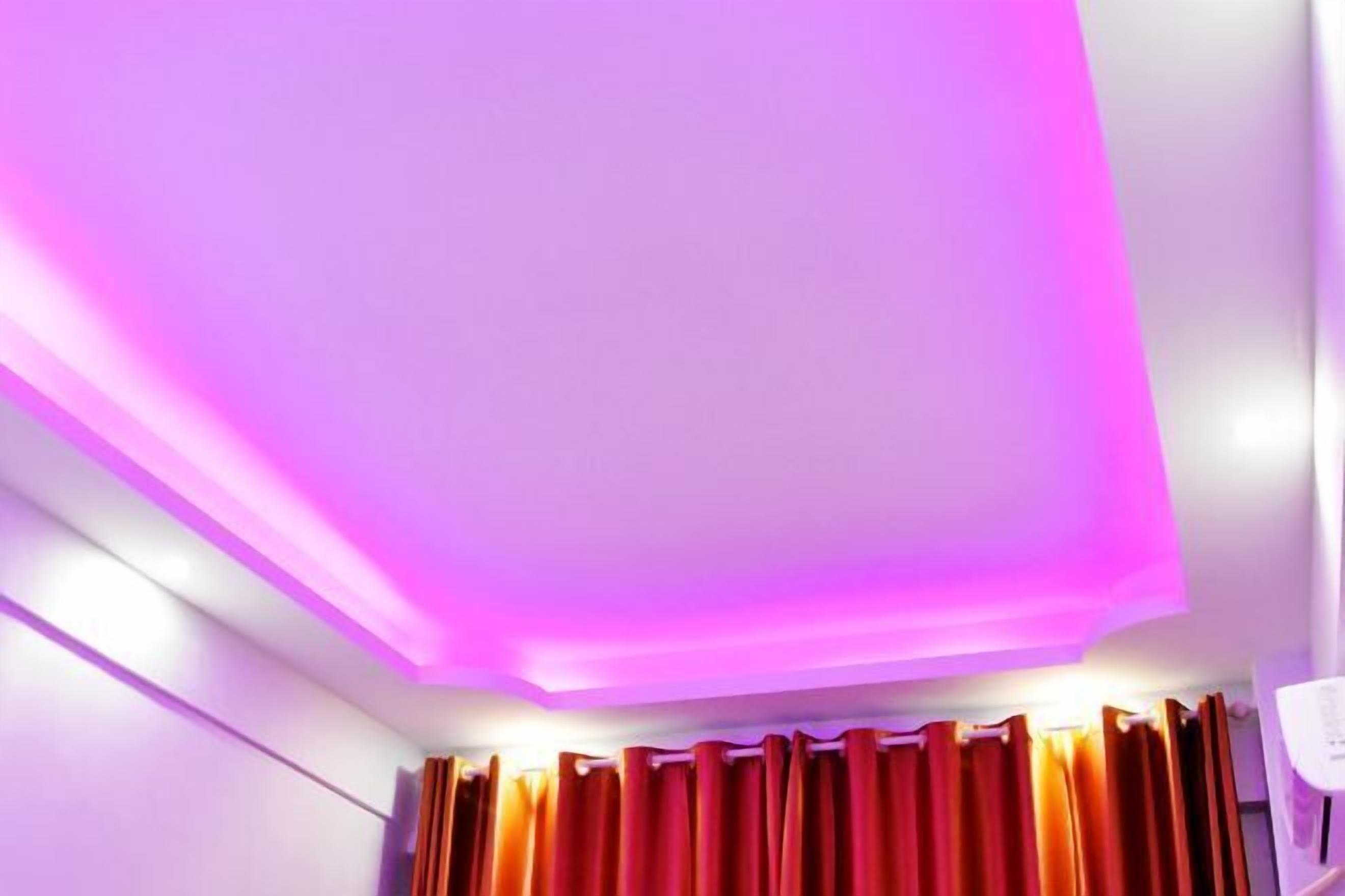 A room with a ceiling featuring a pink LED light strip and a window with red curtains.
