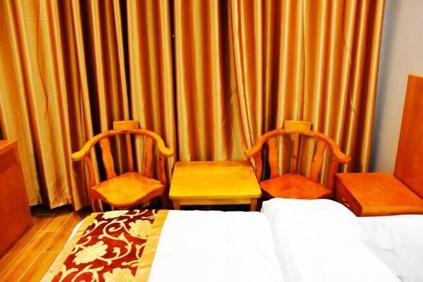 Una habitación de hotel con una cama, dos sillas de madera, una mesita pequeña y un telón de fondo.