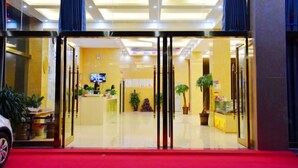 Un hall de hotel con una mesa de recepción, plantas en macetas y una entrada con alfombra roja.