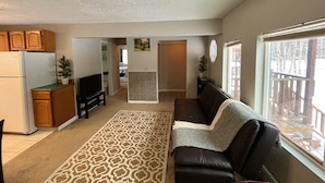 A living room with a sofa, a television, wooden cabinets, and a kitchen area with a refrigerator. - Scenic Alaskan cabin in the mountains (Anchorage)