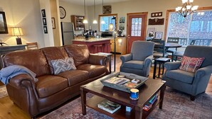 Uma sala de estar acolhedora com um sofá de couro marrom, uma poltrona azul e uma mesa de centro de madeira com revistas e uma caneca azul.