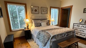 Quarto com uma cama, duas mesas de cabeceira com luminárias, um banco, cômoda com silhuetas de pássaros e impressões botânicas emolduradas na parede.