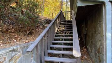 A wooden staircase leading to a stone building, surrounded by trees and fallen leaves.