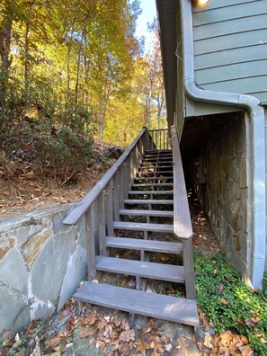 A wooden staircase leading to a stone building, surrounded by trees and fallen leaves. - Red Wolf Lodge-Blue Ridge views, wraparound deck, outdoor fireplace (Dillard)