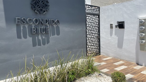 Une entrée d'immeuble avec une enseigne indiquant « ESCONDIDO BIU » et un portail décoratif en métal.