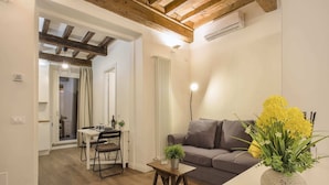 A cozy living room with a wooden ceiling, a grey sofa, a small table with a plant, and a dining area with a white table and chairs. - La Sinagoga Suite (Florence)