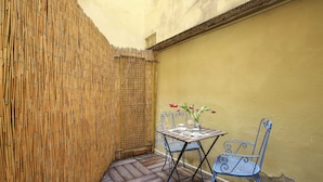 A small outdoor patio with a bamboo fence, a wooden table, two chairs, and a vase with flowers. - La Sinagoga Suite (Florence)