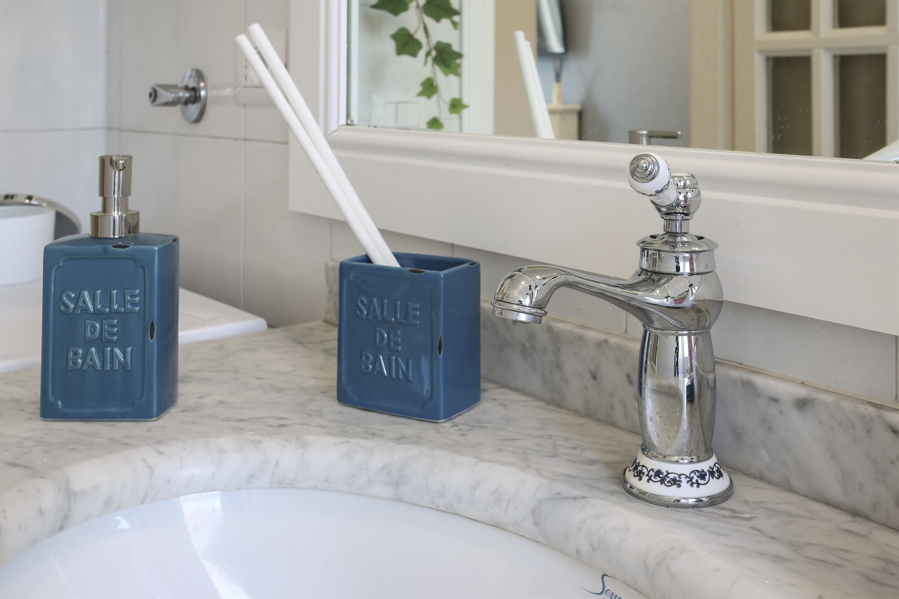 Une salle de bain avec un lavabo blanc, un robinet argenté et deux distributeurs de savon bleus portant l’inscription « SALLE DE BAIN ».