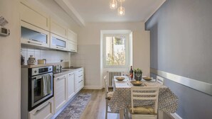 A compact kitchen with white cabinets, a built-in oven, and a dining area with a patterned tablecloth. - Sanzanobi Suite (Florence)