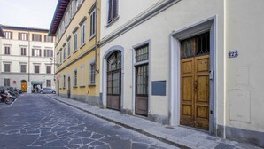 A street with stone pavement, a yellow building with a wooden door, and a sign with the number 122. - Sanzanobi Suite (Florence)