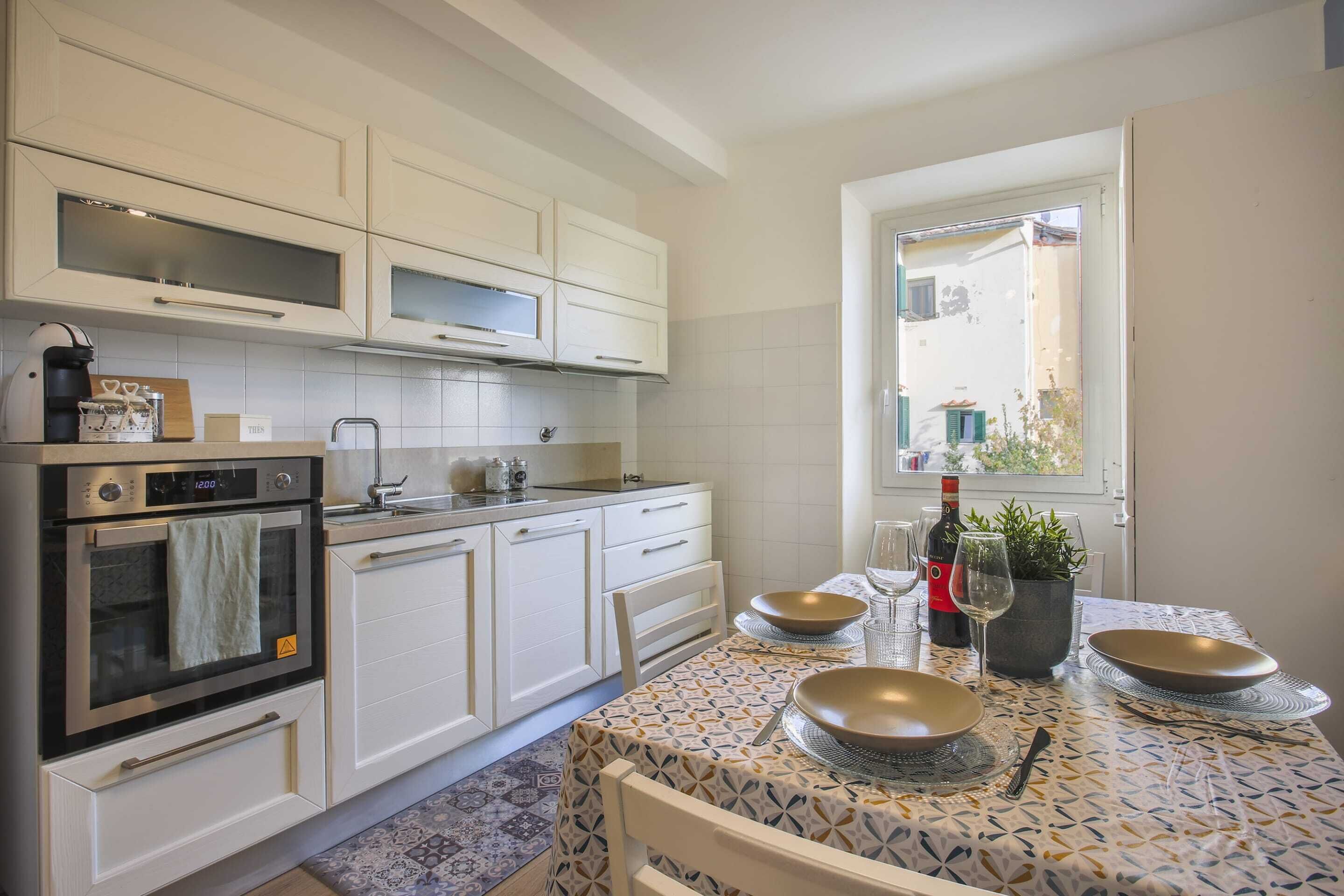 A modern kitchen with white cabinetry, an oven, and a dining table set with plates and a wine bottle.