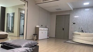 A modern hotel room with a wooden floor, a large bed with grey bedding, a white cabinet, a small trash bin, and a spa tub. - Yurong Shanzhuang Hotel (Nanjing)