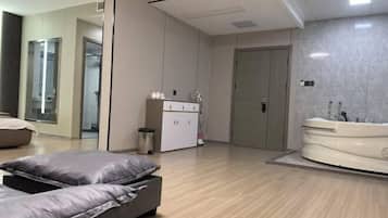 A modern hotel room with a large bed, a separate seating area, a walk-in closet, and a spa-like bathroom with a bathtub.