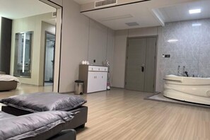 Habitación de hotel moderna con una cama grande, zona de estar independiente, vestidor amplio y un baño estilo spa con bañera.
