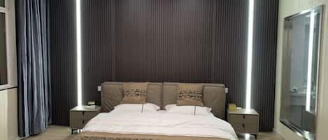 Quarto de hotel moderno com uma cama grande, duas mesas de cabeceira e uma janela ampla.
