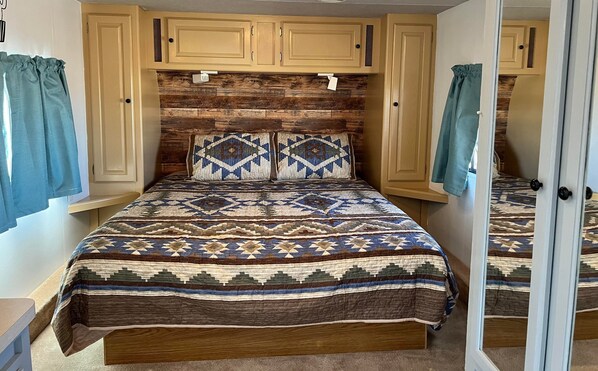 A bedroom with a wooden headboard, a patterned bedspread, and built-in cabinets. - The Desert Oasis Campground (McNeal)