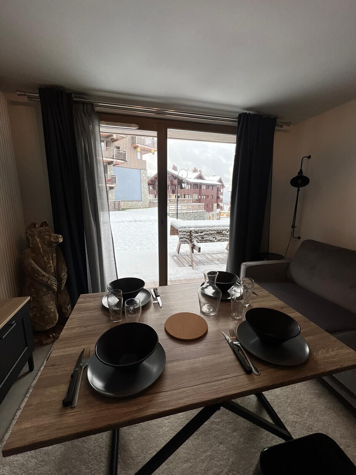 A dining area with a wooden table set for two, a sofa, and a statue.