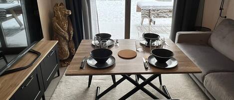 A modern living room with a dining table set for two, a sofa, a TV, and a view of a snowy outdoor area.