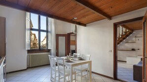 A dining area with a wooden ceiling, white chairs, a table, and a view of the street through large windows. - Santa Maria Novella Bright and Modern Apartment (Florence)