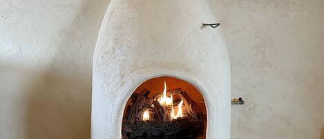 Une cheminée en pierre avec un feu qui crépite à l’intérieur, un climatiseur fixé au mur et un téléviseur posé sur une étagère en bois.